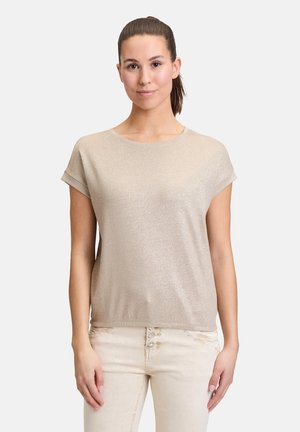T-shirt métallique doré à manches courtes, col rond, coupe décontractée et texture douce, associé à un pantalon ajusté de couleur claire.