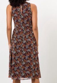 Robe midi sans manches avec un motif floral violet, orange, blanc et vert, taille cintrée, et une petite ouverture en forme de clé dans le dos.