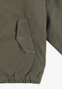 Oliwkowa kurtka z teksturowanej bawełny, z ukośną kieszenią i elastycznym dołem. Prosty, funkcjonalny design z minimalną ilością szwów.