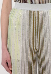Πτυχωτό παντελόνι με φαρδύ ασημένιο ζωνάκι, διακοσμημένο με κατακόρυφες ρίγες σε πράσινο, ασημί και καφέ χρώμα, εμπλουτισμένο με παγιέτες για υφή.