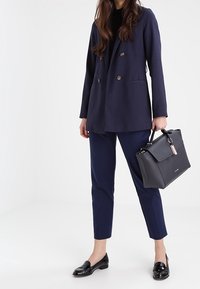 Marineblå dobbeltradet blazer, marineblå tilspidsede bukser, sorte lakloafer og en struktureret sort håndtaske med en pink detalje.