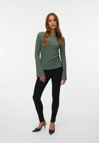 Groene lange mouw top van textuurstof met uitlopende mouwen, gecombineerd met zwarte slim-fit broek en puntige hakken. Eenvoudig, getailleerd ontwerp.