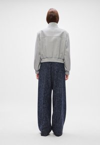 Grijze cropped jas met een hoge kraag en ribbelrand, gecombineerd met wijdvallende donkerblauwe broek van textuur met subtiele spikkels.