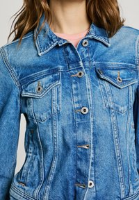 Blue denim jacket with a classic design, featuring silver-tone buttons, two chest pockets, and subtle stitching details.