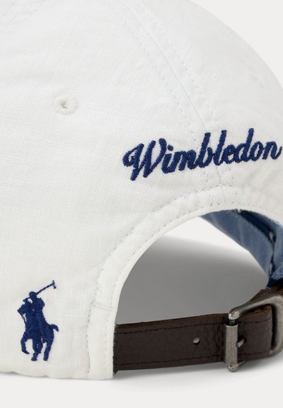 Λευκό καπέλο μπέιζμπολ με κεντημένο το «Wimbledon» σε μπλε και μπλε λογότυπο παίκτη πόλο κοντά στο ρυθμιζόμενο καφέ δερμάτινο λουράκι στο πίσω μέρος.