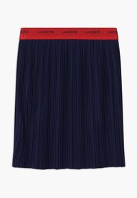 Námořnická plisovaná sukně s širokým  červeným páskem, na němž je vpředu logo "LACOSTE". Vyrobena z lehkého materiálu s hladkým povrchem.