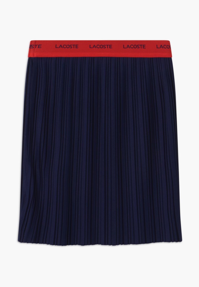 Námořnická plisovaná sukně s širokým červeným páskem, na němž je vpředu logo "LACOSTE". Vyrobena z lehkého materiálu s hladkým povrchem.