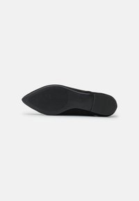 Semelle de chaussure noire à bout pointu avec des motifs de grip texturés au talon et à l'avant-pied, photographiée sur un fond blanc uni.
