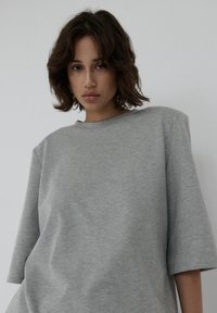 Szara, oversize'owa koszulka wykonana z miękkiego materiału; posiada okrągły dekolt i krótkie rękawy, z nieco luźnym krojem i gładką teksturą.