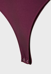 Bordo bikini donji dio visokog kroja s glatkom teksturom, koji ima dvije metalne rupice i čiste šavove za uredan izgled.
