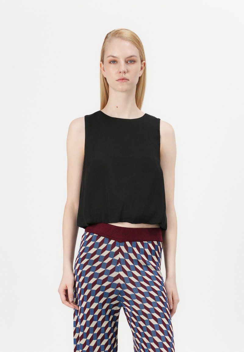 Zwarte mouwloze top met een ronde halslijn, gecombineerd met gestreepte broek met geometrische vormen in rood, blauw en crème kleuren.