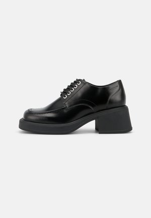 Zwarte leren veterschoen met stevige blokhak en afgeronde neus, zijstiksels en merklogo vlakbij de hiel.