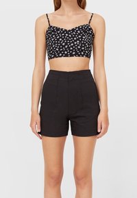 Top corto nero a fiori con spalline sottili abbinato a pantaloni corti neri a vita alta. Tessuto morbido, vestibilità su misura e pieghe verticali sui pantaloni.