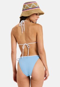 Lichtblauwe bikini met een driehoekig bovenstuk en zijstrikjes, met witte accenten. De geweven rieten emmershatt heeft een band met een meerkleurig patroon.