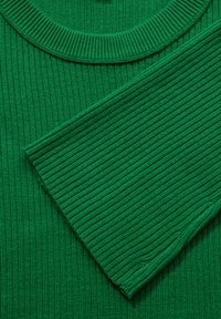 Il tessuto a maglia verde rigato presenta una scollatura rotonda e una disposizione diagonale delle maniche, evidenziando la sua superficie strutturata e il colore uniforme.