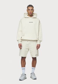 Gaišbeige hoody un šortu komplekts, kokvilnas materiāls, priekšējais kabata hoody, "PEGADOR" melns logo, apvienots ar pelēkiem sporta apaviem un balt�ām zeķēm.