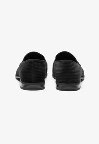 Schwarze Slippers mit gerippter Textur, runder Spitze und flachen Absätzen. Verfügt über ein glattes Rückendesign und minimalistische Akzente.
