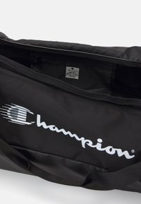 Bolso de deporte negro hecho de material duradero con cierre de cremallera. Presenta un logotipo de Champion en blanco y una etiqueta en el interior. Tamaño: Talla única.