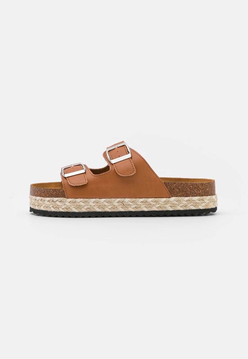 Bruine leren slippers met twee verstelbare gespen, voorzien van een geweven jute tussenzool en een zwarte rubberen loopzool voor grip.