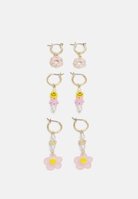 Três pares de brincos com argolas douradas, flores cor-de-rosa e charms de donut, carinhas sorridentes amarelas e detalhes em pérolas. Formas e designs variados.
