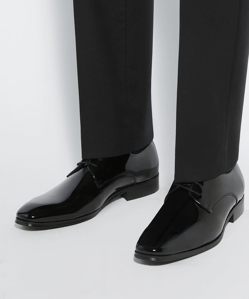 Chaussures habillées en cuir noir poli avec lacets portées avec un pantalon formel noir sur un fond uni clair.