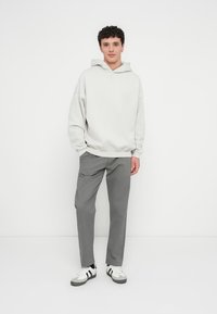 Light gray hoodie with a relaxed fit, paired with gray trousers and white sneakers featuring black accents. Simple, modern design.