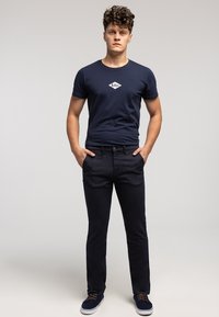 Granatowa koszulka z okrągłym dekoltem i białym logo w kształcie diamentu, zestawiona z ciemnymi dżinsami. Niech niebieskie sneakersy z białymi podeszwami dopełnią stylizację.