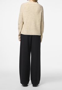 Pull beige en maille avec une coupe décontractée, manches raglan et dos court, associé à un pantalon noir taille haute à jambes larges.