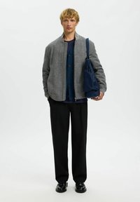 Hallhallisest herringbone mustri bomber-jakk mustade aktsentidega sinise kardiganiga, kaasas mustad püksid ja tumehall köitmisega kott.