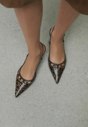 Legs wearing pointed-toe slingback flats with brown and black leopard print on light gray textured floor.