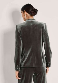 Samtblazer in Dunkelgrau mit tailliertem Schnitt, Spitzrevers und geknöpften Ärmelbündchen. Glatte Textur mit dezentem Glanz und klaren Linien.