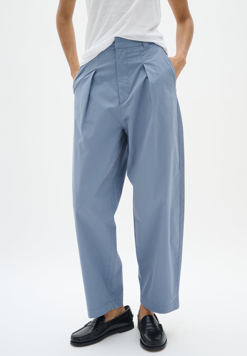 Lichtblauwe wijde broek met voorplooien, zijzakken en een zachte, lichte textuur, gecombineerd met zwarte instappers.