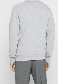 Sudadera gris con puños y dobladillo acanalados, que presenta un cuello redondo clásico y una textura suave. La parte posterior muestra mangas raglán sin costuras.