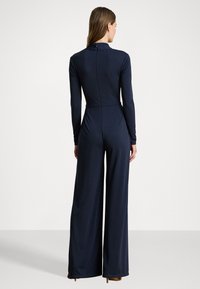 Navy blue long-sleeve jumpsuit with fitted bodice and wide-leg pants. Features a high collar and a back zipper closure. Soft, stretchy fabric.