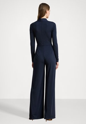 Jumpsuit lungo blu navy a maniche lunghe con corpino aderente e pantaloni a gamba ampia. Presenta un alto colletto e una chiusura con zip sul retro. Tessuto morbido e elasticizzato.