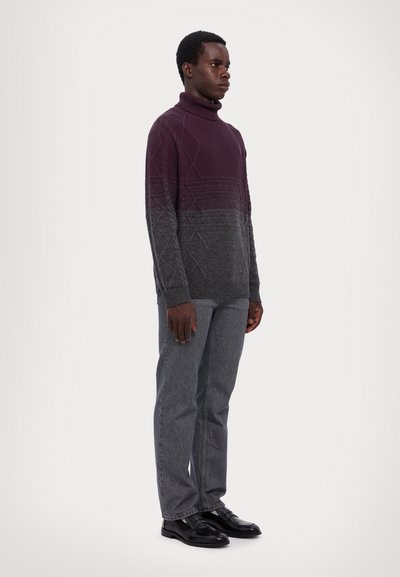 Pull à col roulé en tricot dégradé de bordeaux à gris, avec des motifs texturés. Porté avec un pantalon gris et des chaussures noires.