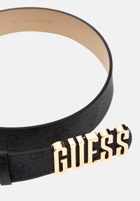 Cintura in pelle nera con fibbia logo "GUESS" in tonalità oro. Superficie testurizzata con fodera interna liscia. Taglia regolabile.