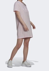Růžové bavlněné šaty s krátkým rukávem, s vyšitým logo Adidas na přední straně. Nosí se s bílými sportovními botami.