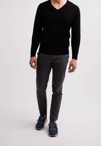 Schwarzer V-Ausschnitt-Pullover mit langen Ärmeln, kombiniert mit schmal geschnittenen grauen Hosen und navy-blauen Sport Schuhen mit hellgrauen Akzenten und Schnürsenkeln.