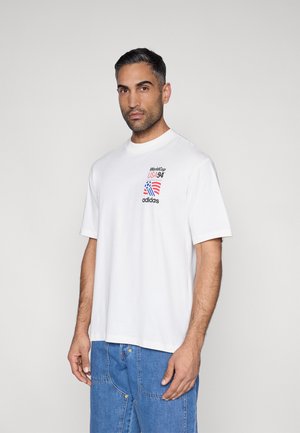 Wit katoenen T-shirt met de opdruk "World Cup USA 94", een ontwerp van de Amerikaanse vlag en het "adidas"-logo in rood en blauw. Korte mouwen, ronde hals.