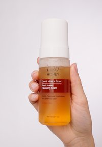 Reinigingsschuim in een doorzichtige fles met een witte pompdeksel. Amberkleurige vloeistof, etiket met rode accenten, tekstdetails en aangegeven capaciteit van 150 ml.