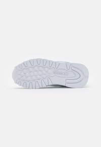 Semelle de sneaker Reebok, en caoutchouc blanc avec des motifs texturés et des grips circulaires ; présente une légère courbure et un logo au centre.