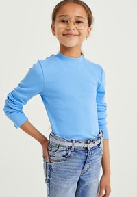 Világoskék bordázott, hosszú ujjú póló magas gallérral, elhalványult kék farmerral és ezüst színű övvel párosítva.