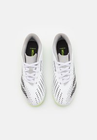 Zapatos de fútbol blancos con parte superior texturizada y detalles en negro y verde neón, diseño de puntera redonda y cierre de cordones estándar.