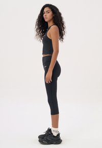 Zwarte sportieve cropped top en hoge taille legging, gecombineerd met zwarte sneakers en witte logo sokken. Glad stof, aansluitend ontwerp.