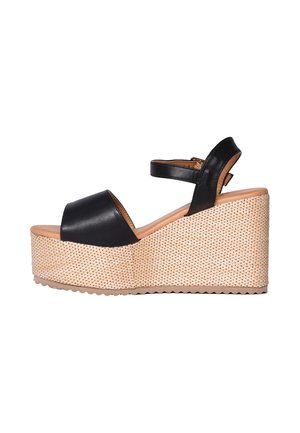 Sandalo con zeppa in pelle nera con cinturino alla caviglia e suola platform intrecciata su sfondo bianco.