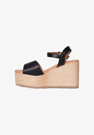 Sandalo con zeppa in pelle nera con cinturino alla caviglia e suola platform intrecciata su sfondo bianco.