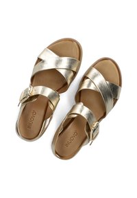 Gouden metallic sandalen met kruislings banden, een gespsluiting en een bruine leren voetbed. Plat ontwerp voor optimaal comfort.