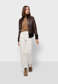 Braune Leder-Bomberjacke mit gerippten Bündchen, beiger Rollkragenpullover und weißen weit geschnittenen Jeans. Braune Schnürstiefel mit strukturierten Sohlen.