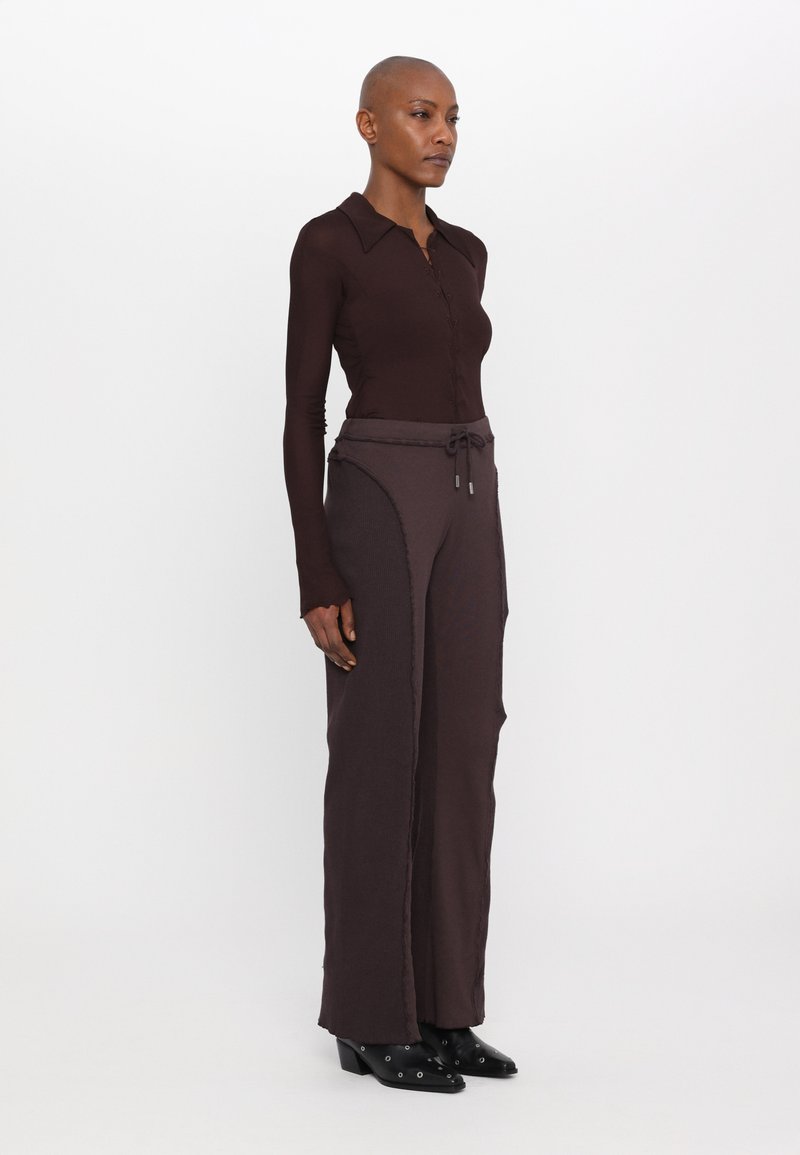 Blusa de manga larga color marrón oscuro con botones al frente; pantalones anchos a juego con cintura ajustable y detalles en las costuras laterales. Botines negros de tacón.